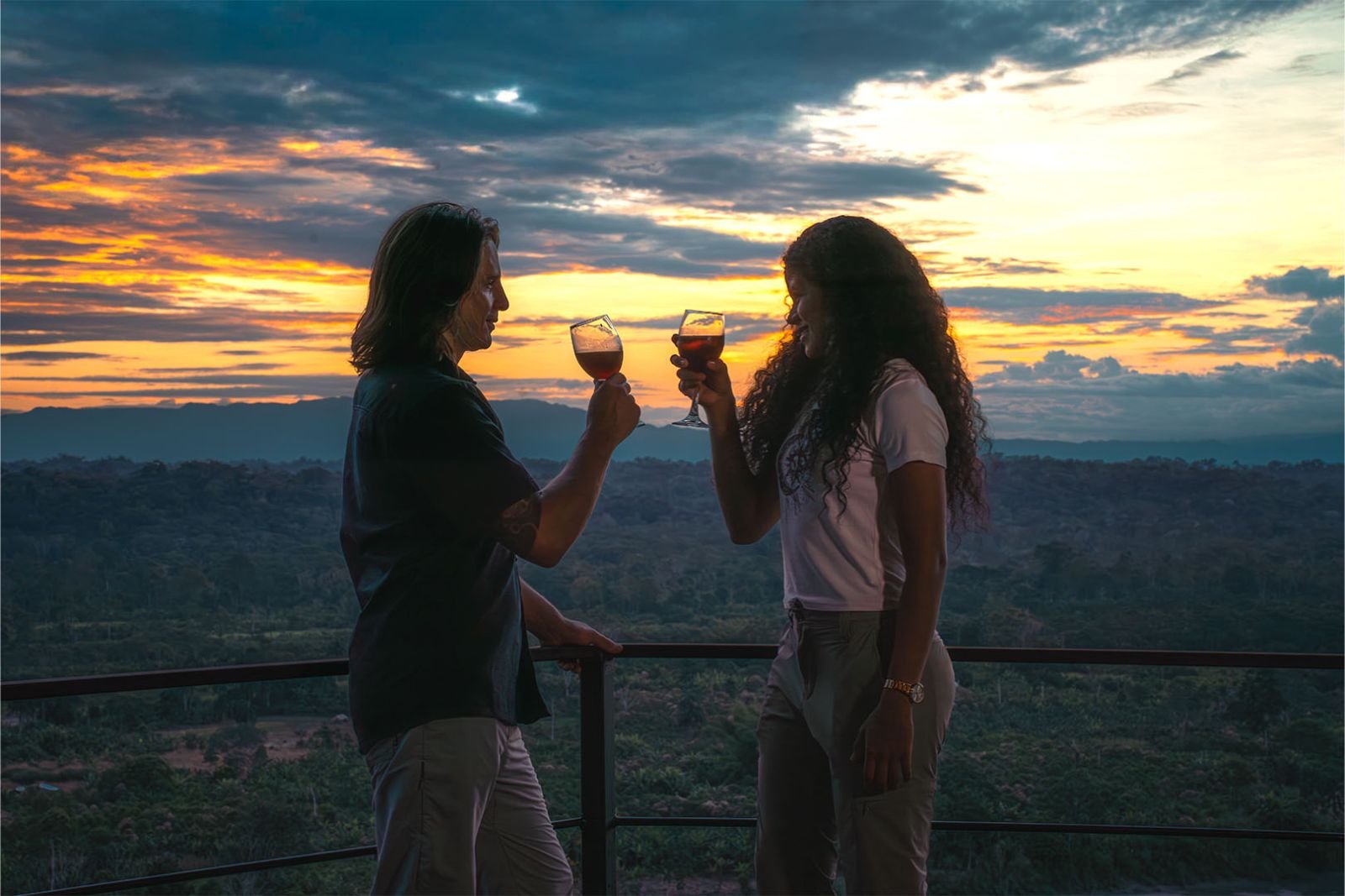 Pareja brindando en la baranda al atardecer, sobre la selva