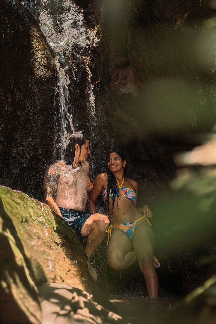 Pareja bajo el salto de agua, entre rocas cubiertas de musgo