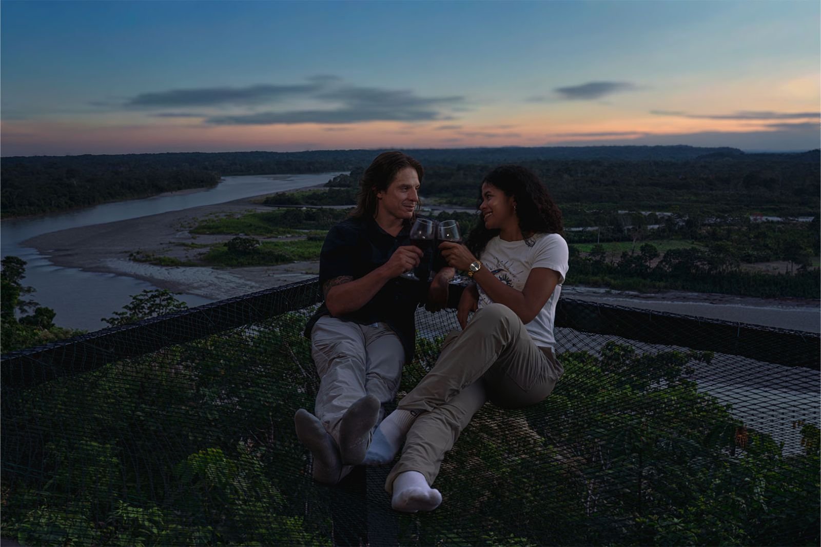 Pareja brindando sobre la red suspendida, con el Río Napo al atardecer