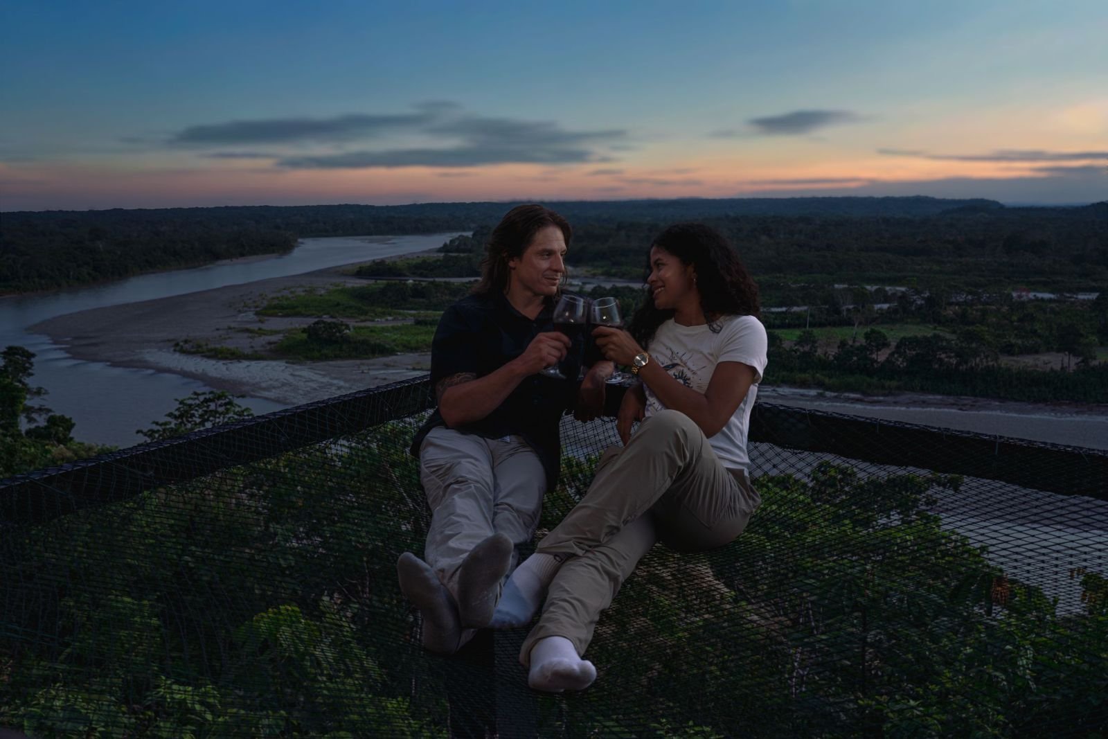 Pareja brindando sobre la red suspendida, con el Río Napo al fondo
