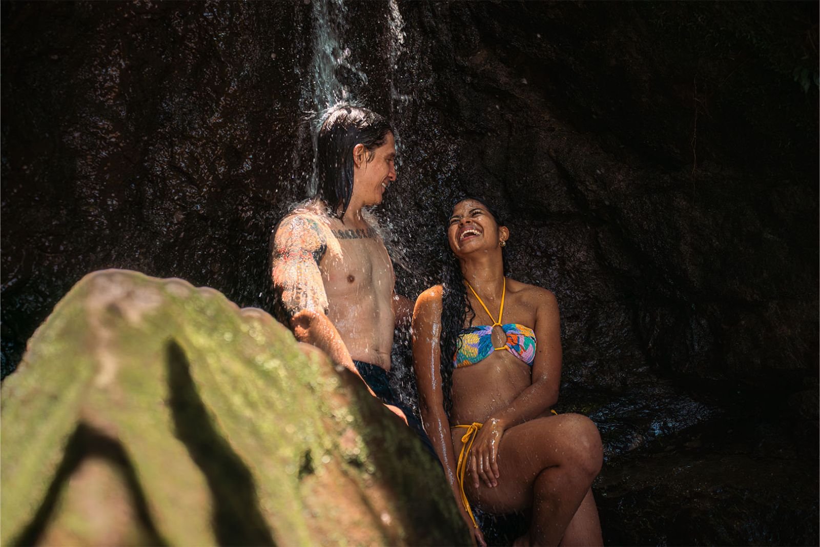 Pareja riendo bajo una cascada peque&ntilde;a entre rocas