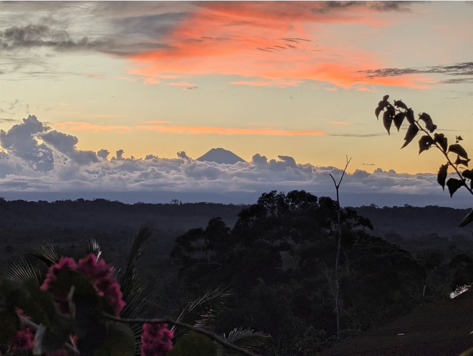 Atardecer con un volcán de los Andes sobre las nubes y la selva